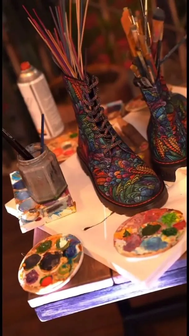 Hand-painted patterned boot surrounded by brushes and paint palettes at a live-art activation