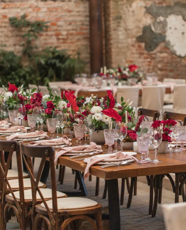 Mesas de banquete de boda con servilletas rosas y flores rojas y blancas en un patio rústico