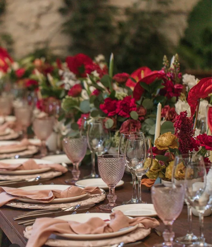 Montaje de boda con servilletas rosas, copas rosas y un camino de flores rojas