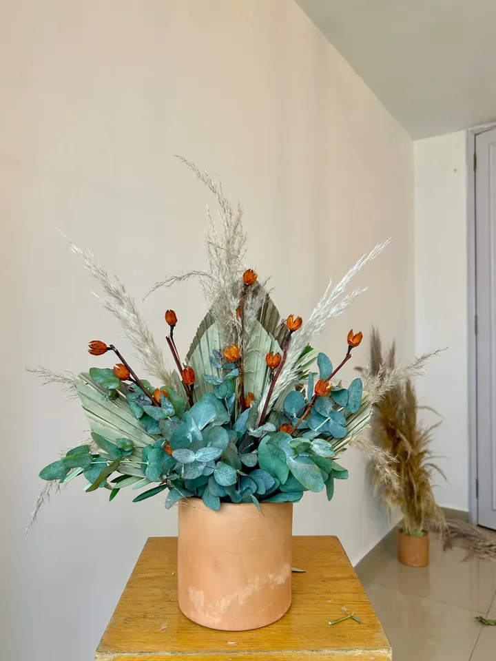 Arreglo de flores secas con eucalipto, pampa y flores naranjas en una maceta de barro