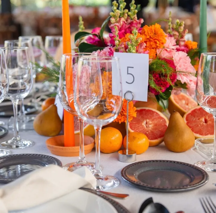 Mesa de boda colorida con cítricos, zinnias y velas naranjas, y un número de mesa 5