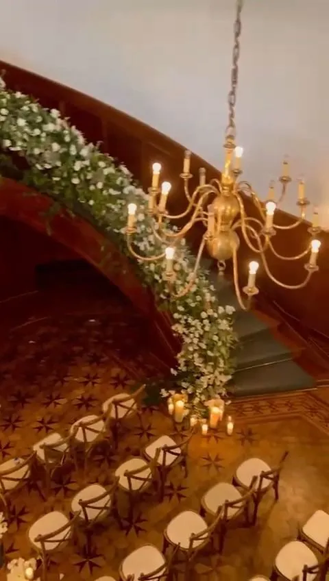 Escalera curva decorada con flores blancas sobre el pasillo de una ceremonia, iluminada por una lámpara dorada