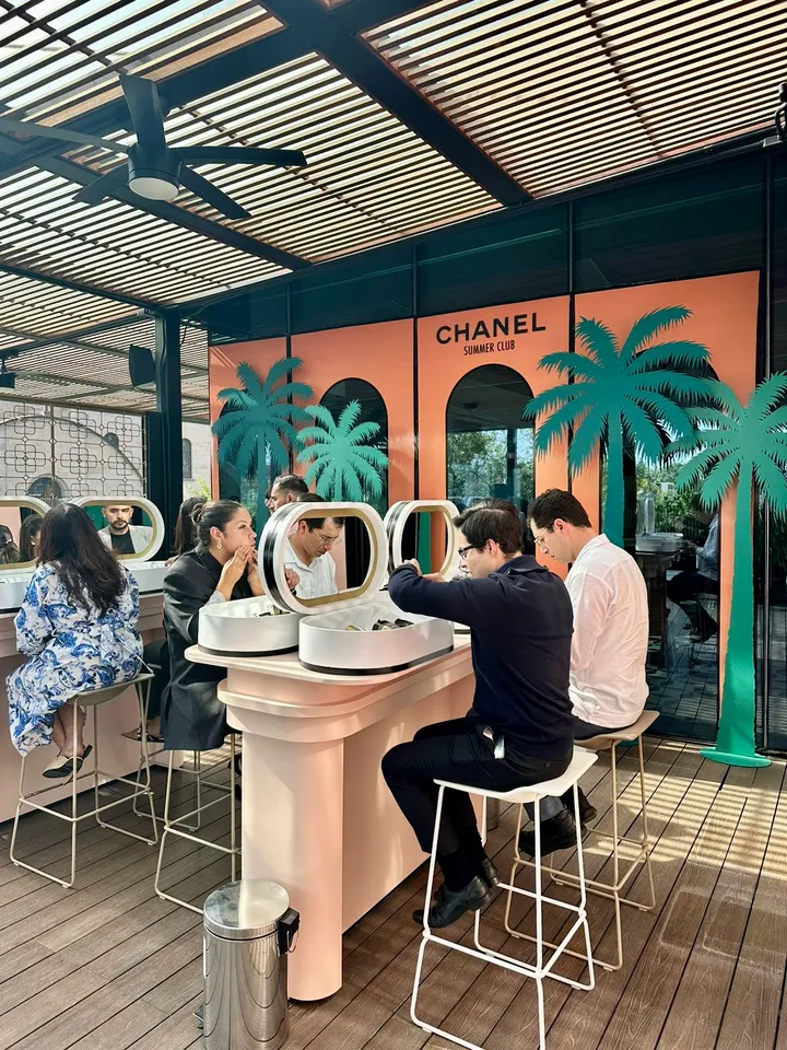 Guests at a lit-mirror beauty station on the Chanel Summer Club terrace with palm-tree wall graphics