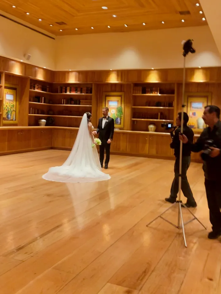 Novia con velo largo y novio posando para un fotógrafo en una sala revestida de madera