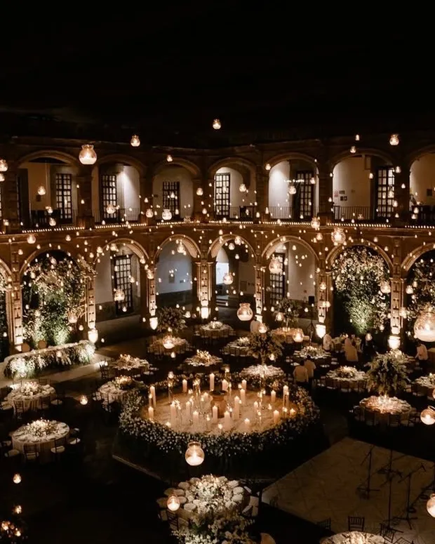 Grand candlelit wedding reception in a historic arched courtyard with string lights and white florals