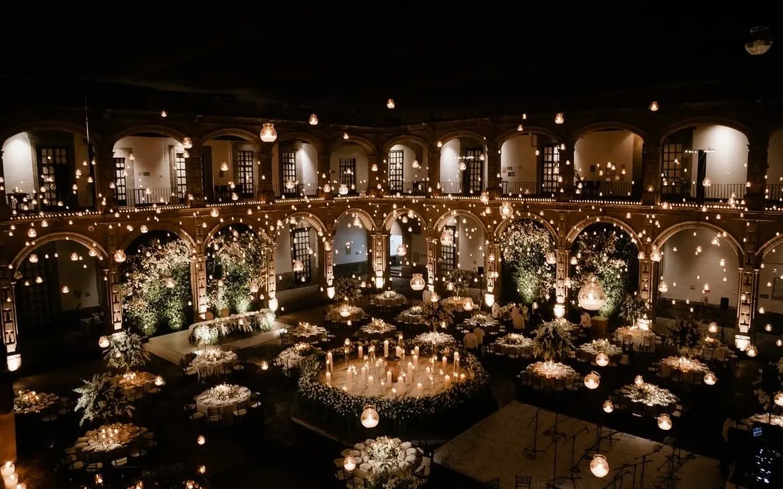Gran banquete de boda a la luz de las velas en un patio histórico con arcos, guirnaldas de luces y flores blancas