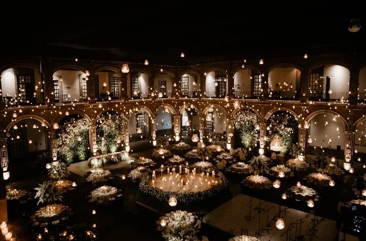 Gran banquete de boda a la luz de las velas en un patio histórico con arcos, guirnaldas de luces y flores blancas
