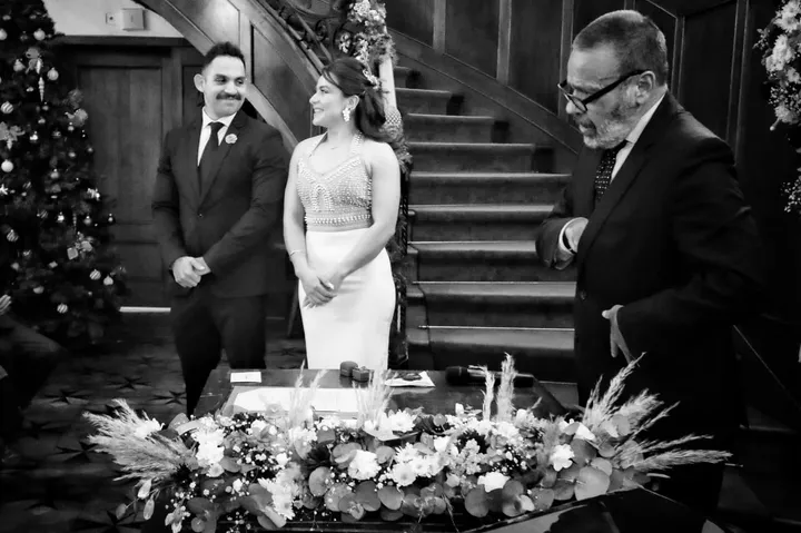 Foto en blanco y negro de los novios riendo con el oficiante en su ceremonia de boda