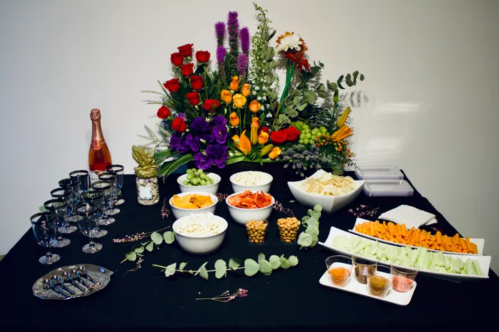Mesa de catering con un gran centro floral, cuencos de aperitivos, crudités y vino espumoso