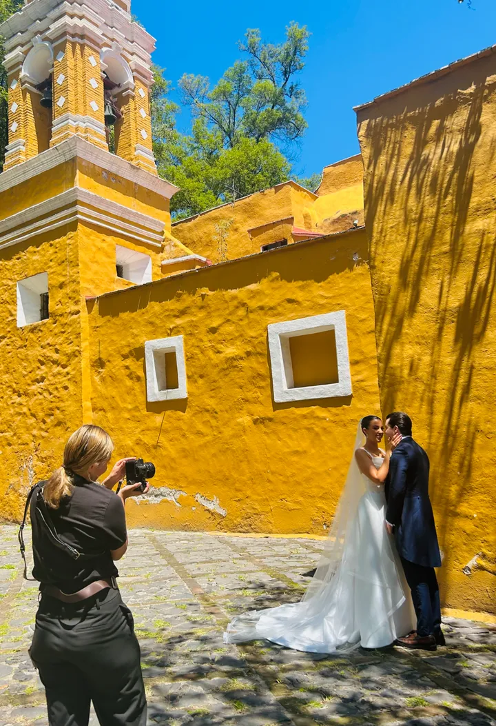 Pareja besándose ante un muro colonial amarillo mientras una fotógrafa los retrata