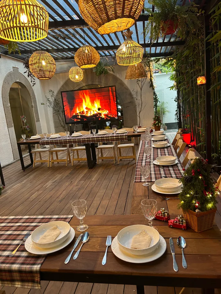 Mesa de cena en terraza cubierta con caminos de cuadros, lámparas de mimbre y una pantalla de chimenea