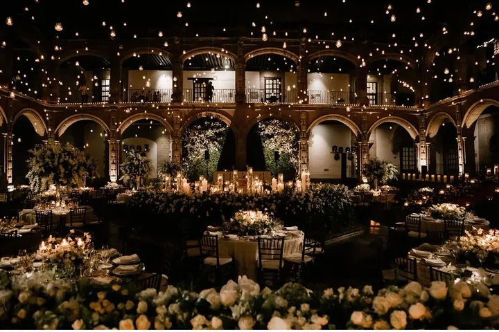 Mesas redondas de boda bajo un dosel de luces en un patio histórico con galerías