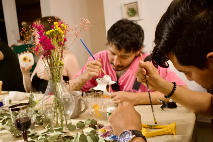 Invitados pintando pequeñas figuras de cerámica con pinceles finos en un taller nocturno
