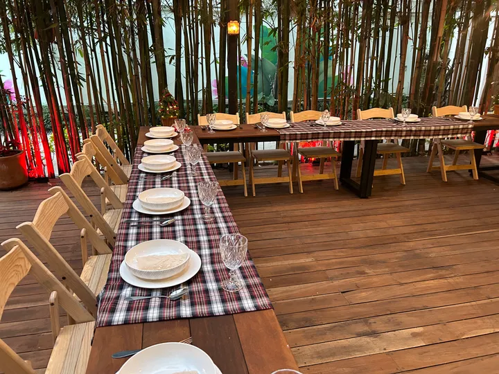 Mesas largas de madera con caminos de cuadros y platos blancos ante un fondo de bambú