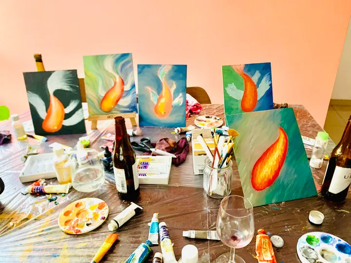Hilera de cuadros de peces koi en caballetes en un taller de pintura con vino, con pinturas y copas