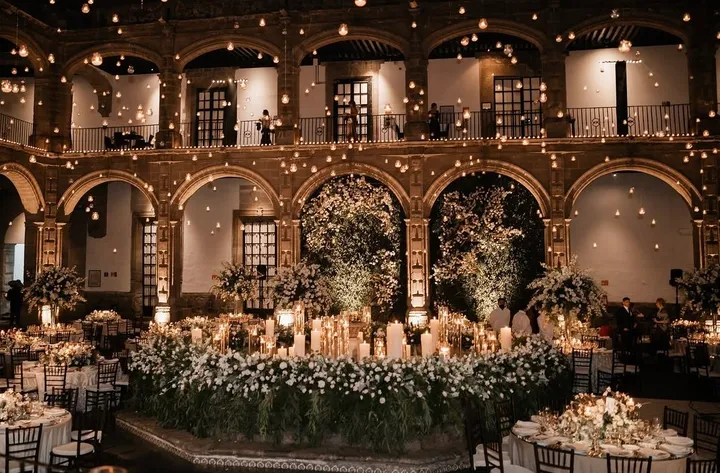 Mesas de boda a la luz de las velas con flores blancas en un gran patio de piedra con arcos