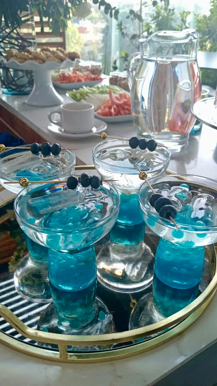 Bandeja dorada con cócteles azules y brochetas de arándanos en una mesa de catering