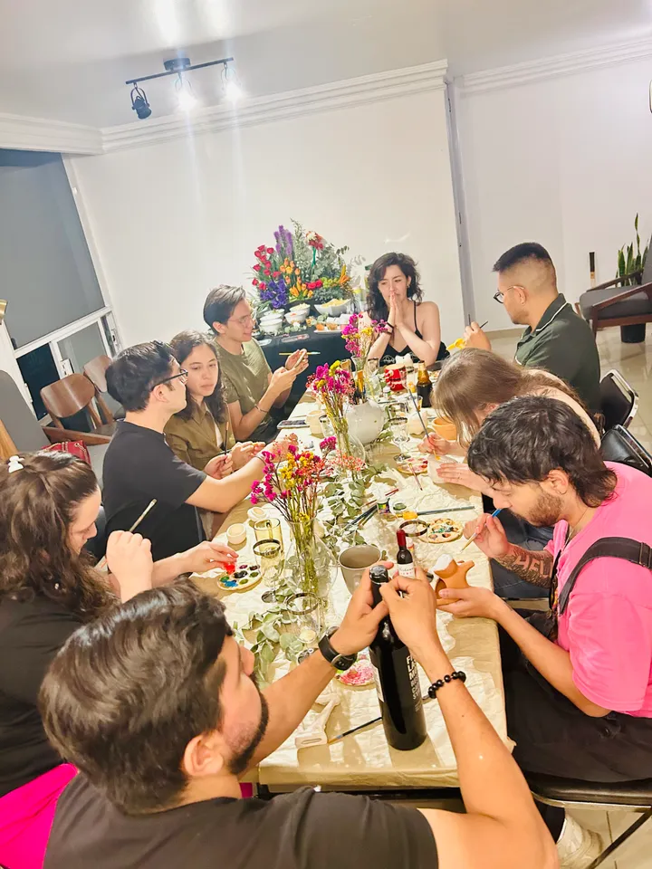 Invitados en una mesa larga con flores, pintando y socializando en una cena-taller