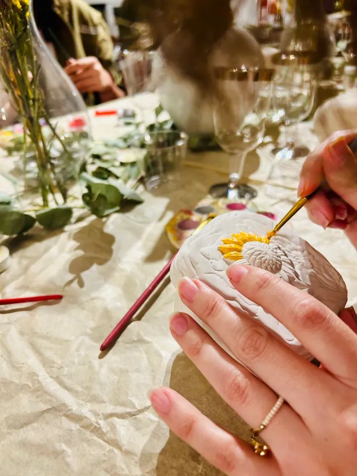 Una mano pintando un girasol sobre una piedra en un taller creativo de mesa