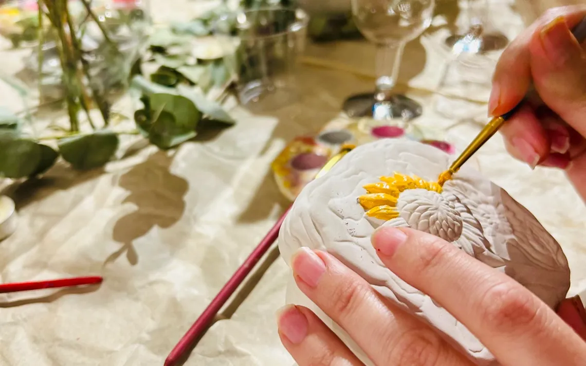 Una mano pintando un girasol sobre una piedra en un taller creativo de mesa
