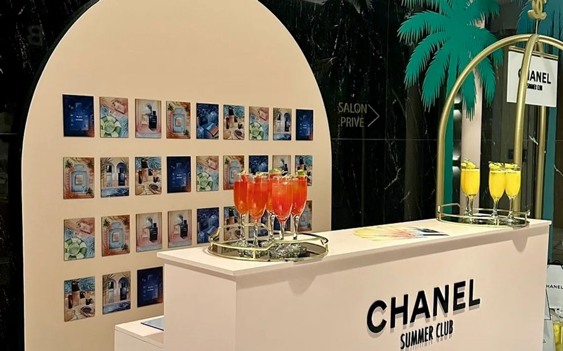 Chanel Summer Club branded pop-up bar with an archway, a wall of colourful prints and orange welcome cocktails