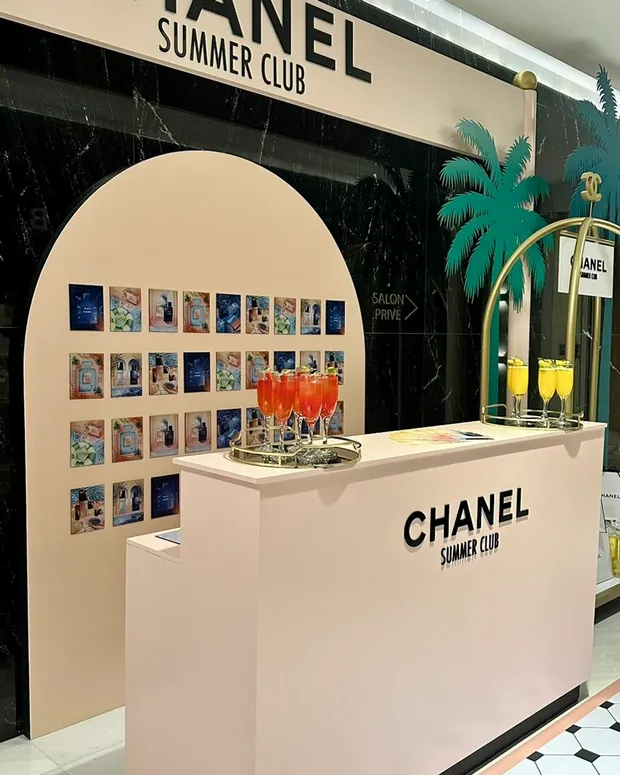 Chanel Summer Club branded pop-up bar with an archway, a wall of colourful prints and orange welcome cocktails