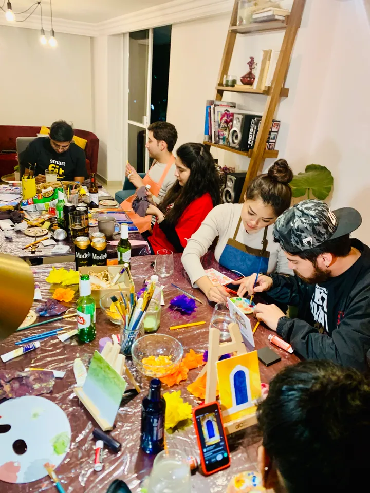 Grupo en un taller nocturno de manualidades decorando casitas de papel en una mesa llena de materiales