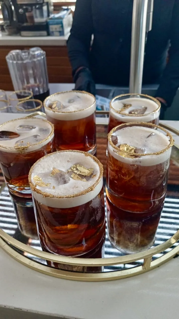 Bandeja dorada con cócteles oscuros de espuma con borde dorado servidos en un evento